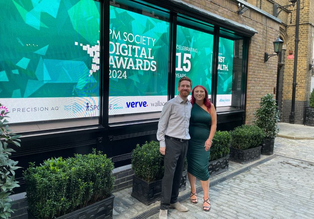 Ellie and Craig stand next to signage for PM digital awards 2024