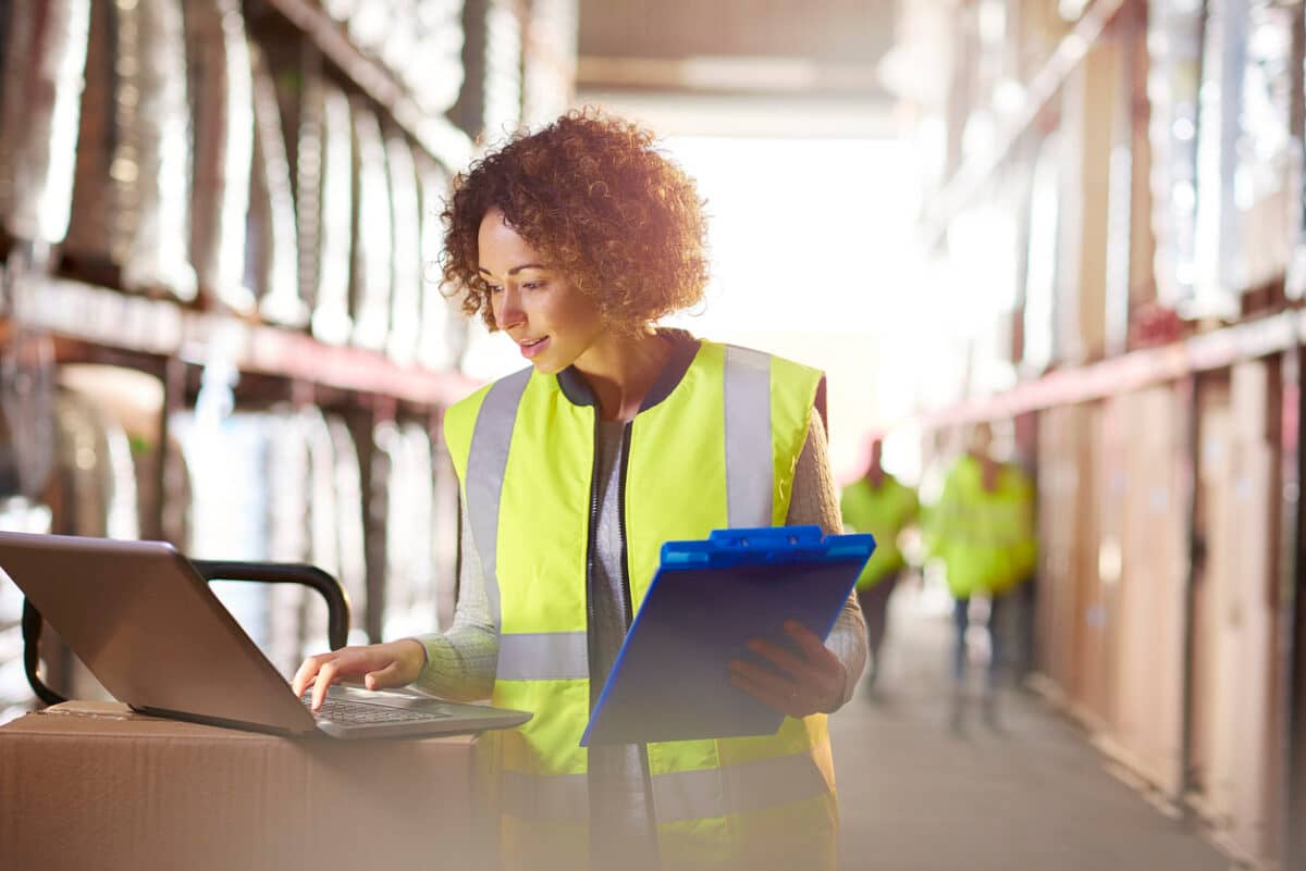 Female warehouse manager looks at stock on a laptop and delivery sheet