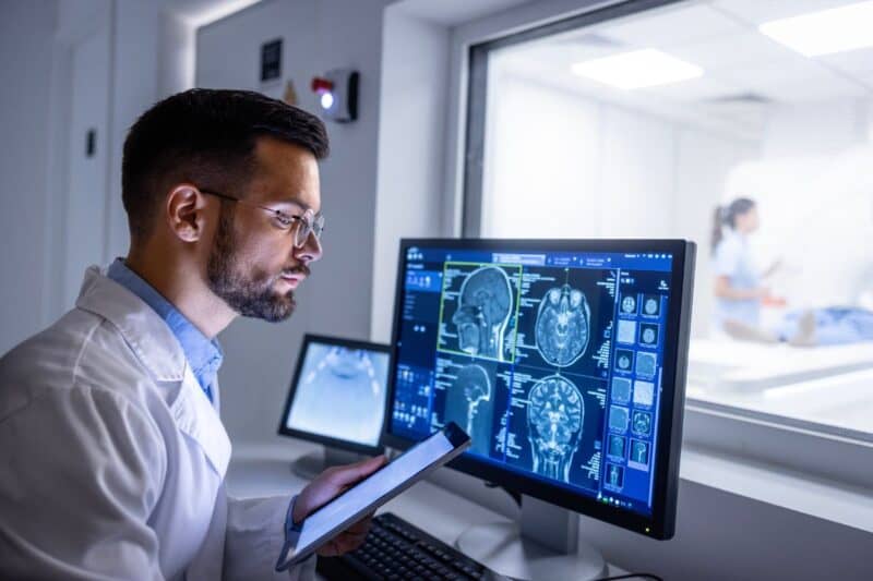 A healthcare professional looking at an MRI scan on a computer and tablet